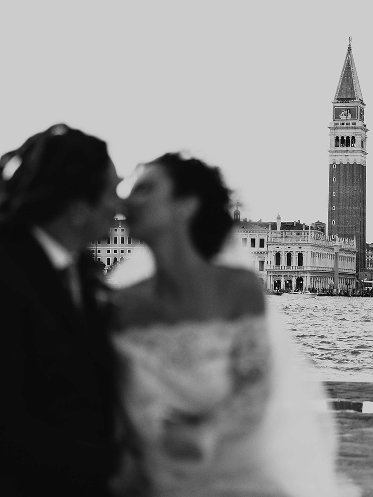 Venice Destination Wedding: a bride and a groom kissing in front of St. Mark's Square